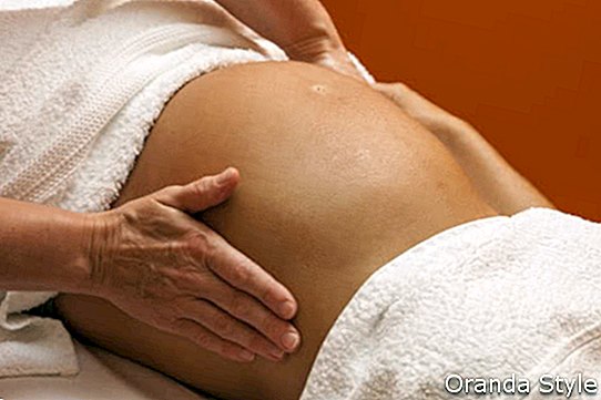Giovane donna latina incinta che si trova su un letto e che ha un massaggio prenatale di rilassamento
