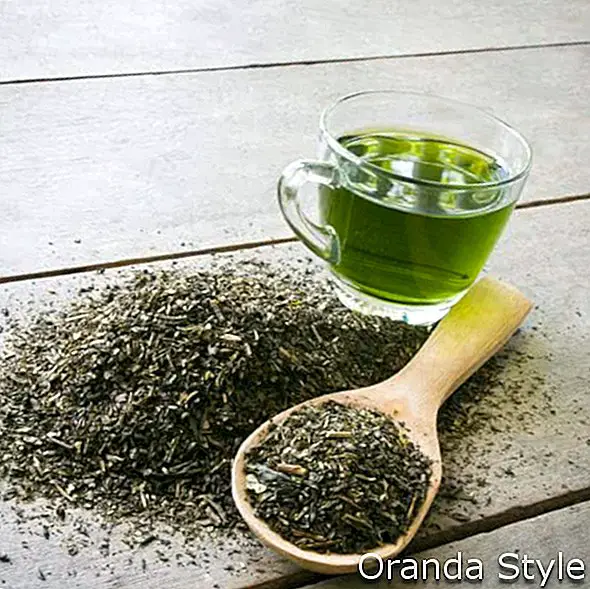 чаша зелен чай и лъжица изсушени листа от зелен чай на дървен фон