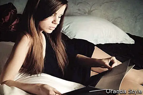 Ung kvinde på sengen læser et magasin