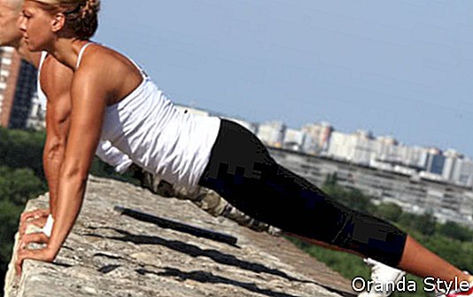 Női és férfi fitness oktatók csinálnak pushups a kőfal tetején