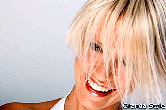 Lebhafte junge Frau mit einer modischen blonden Frisur, die ihr kurzes Haar in der Luft schnippt