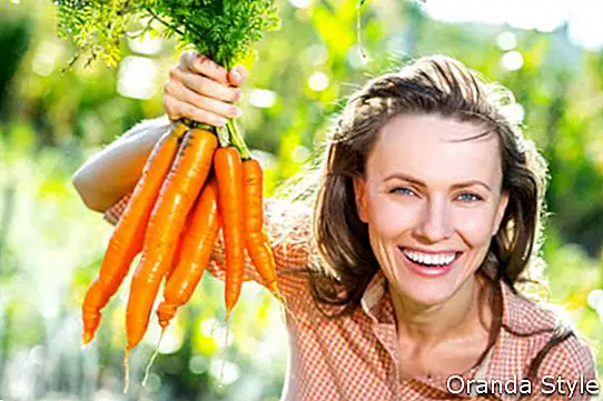 Schöne junge Frau mit organischen Karotten in einem Gemüsegarten