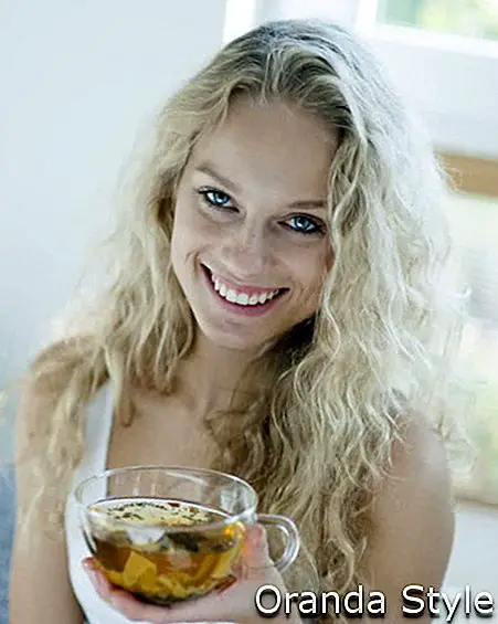 Porträt der glücklichen jungen Frau, die Kräuterteeschale im Haus hält