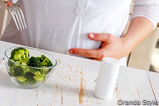 Schwangere Frau, die zwischen Brokkoli und Vitaminen wählt