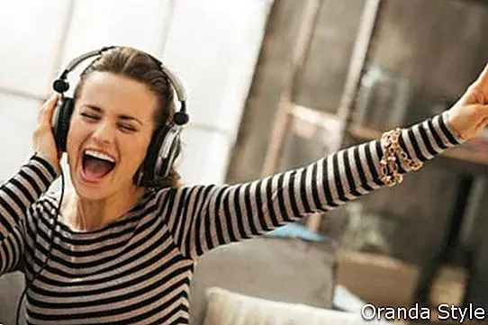 Glad ung kvinde lytter musik i hovedtelefoner i loft lejlighed