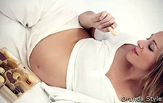 Schwangere Frau, die Plätzchen im Bett isst