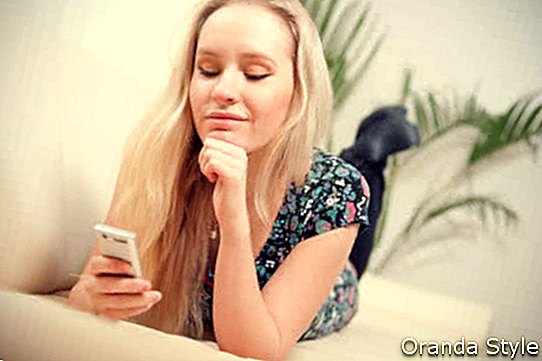 fiatal nő használ mobiltelefon, miközben otthon a kanapén fekszik
