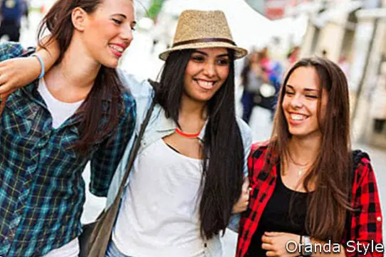 Trys laimingos moterys, einančios mieste, kalbasi viena su kita ir šypsosi