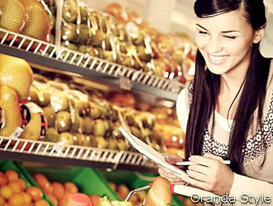 hübsche Frau, die Produkte im Supermarkt mit Liste von Sachen wählt, um zu kaufen