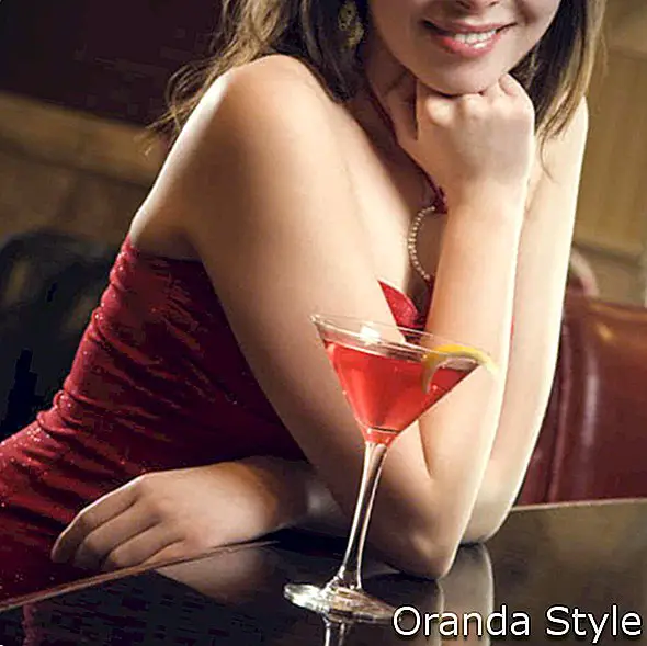 доросла жінка в червоній сукні, посміхаючись і стоячи в барі з напоєм