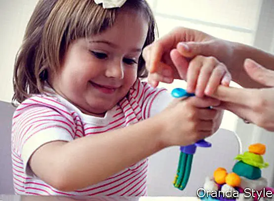 Kleines Mädchen lernt, bunten Spielteig zu benutzen