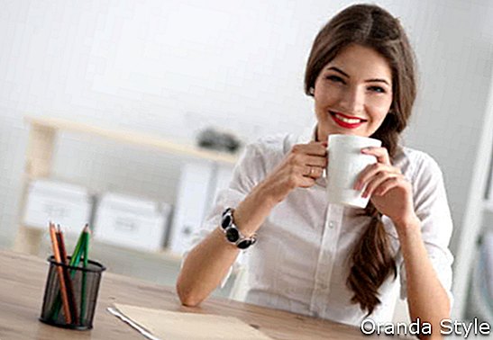 Junge Geschäftsfrau, die auf dem Schreibtisch mit mit Cup sitzt