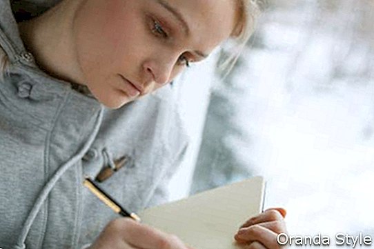 Schreiben des jungen Mädchens in ihrem Tagebuch beim Sitzen an einem großen Fenster