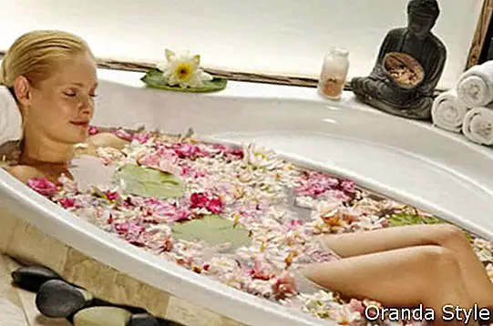 Frau, die im Bad mit dem Blumenblatt sich entspannt