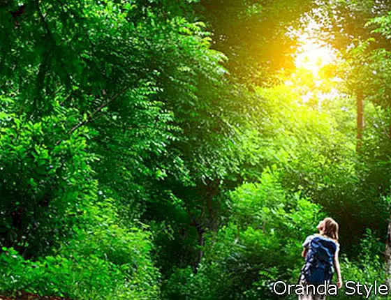 Wanita muda berjalan di jalan asfalt hijau di hutan