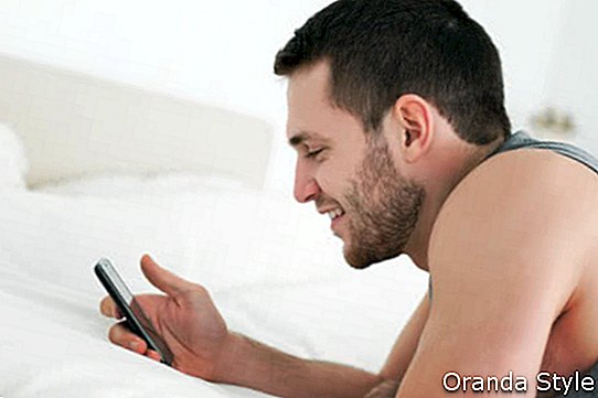 Човек използва мобилния си телефон в спалнята си