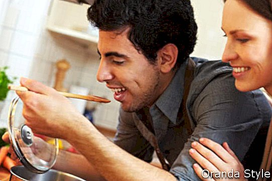 Bemannen Sie Probierensuppe auf einem Ofen in der Küche, während glückliche Frau aufpasst