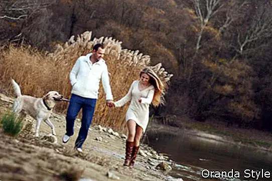 Junges glückliches Paar, das mit Hund nahe dem See im Herbst geht