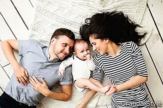 Giovane madre felice del padre e neonato sveglio che si trovano sul pavimento di legno rustico