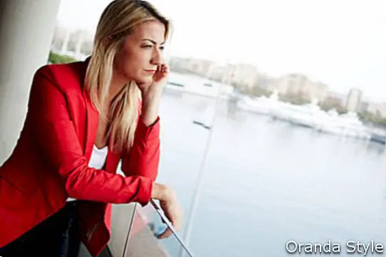 Porträt der nachdenklichen Geschäftsfrau schauend aus einem Bürobalkon mit schöner Seehafenansicht über Hintergrund heraus