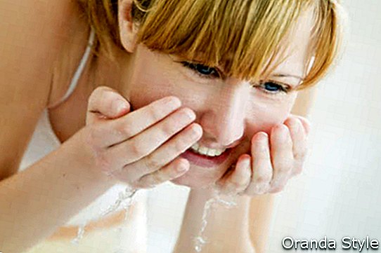 fiatal nő mosás arcát egy mosdóban, és nézi magát a tükörben