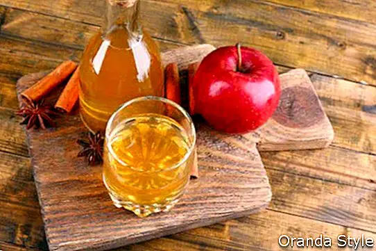 Apfelwein in der Glasflasche mit Zimtstangen und frischen Äpfeln auf Schneidebrett