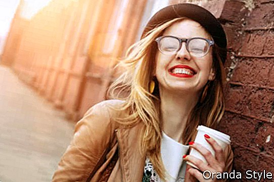 Весела жена на улици пије јутарњу кафу на сунчевом светлу
