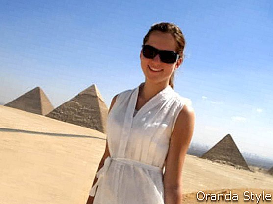 wanita muda yang gembira berdiri di hadapan piramid Mesir di giza