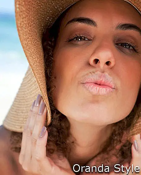 Ung kvinna som bär en sugrörhatt medan hon puckar hennes läppar framför havet