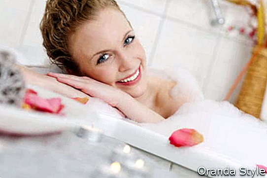 Graži moteris atsipalaiduoja putojoje burbulinėje vonioje, ilsisi galvą ant šono ir šypsosi