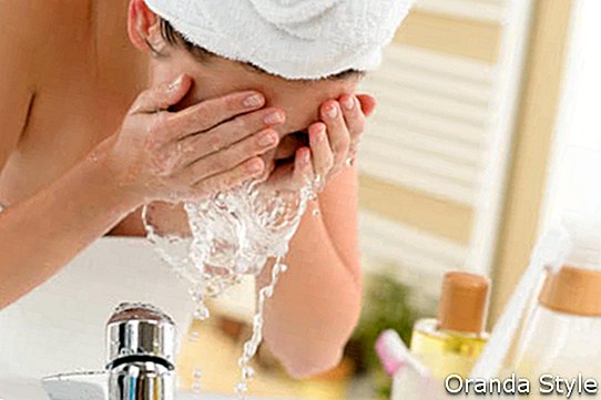 Kvinne som spruter ansiktet med vann over baderomsvasken