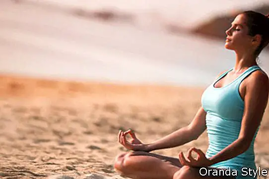 Млада красива здрава жена, правеща медитация на плажа