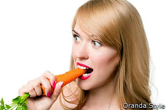 Млада щастлива жена, ядеща моркови