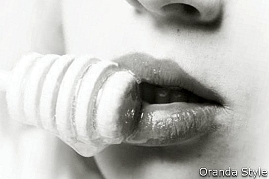 Vista de cerca de los labios de una mujer atractiva mientras come miel de un palo
