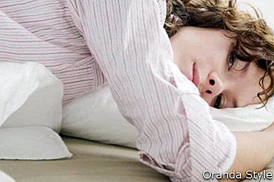 atraktivna zamišljena žena brineta curl s jastukom na krevetu