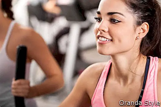 Smukke latinske unge kvinder, der træner i en elliptisk træner i et motionscenter