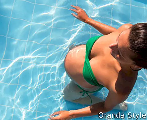 Das schöne Sonnenbräunen der schwangeren Frau entspannte sich am blauen Pool mit grünem Bikini