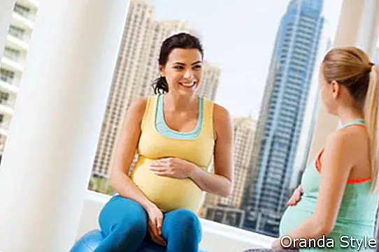 zwei glückliche schwangere Frauen, die auf Bällen in der Turnhalle sitzen und sprechen