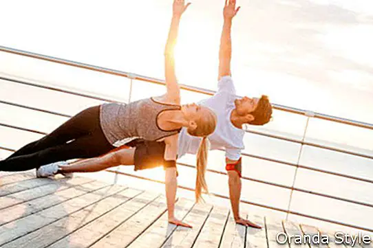 Das lächelnde Paar, das Yoga tut, trainiert draußen am Strandpier