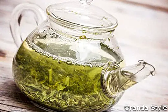 Glasteekanne mit grünem Tee auf Holztisch