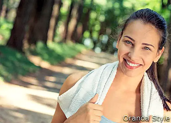 Portree noor atraktiivselt naeratav sobilik naine valge rätikuga, mis puhkab pärast treeningut spordipuhkustes õues pargipuude taustal