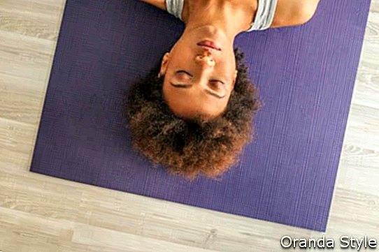 Der Innenhochwinkelschuß einer Afrikanerin, die auf einer Yogamatte mit ihren Augen liegt, schloss