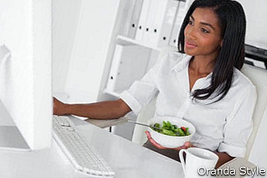Selamat perniagaan wanita cantik yang memakan salad di mejanya di pejabatnya