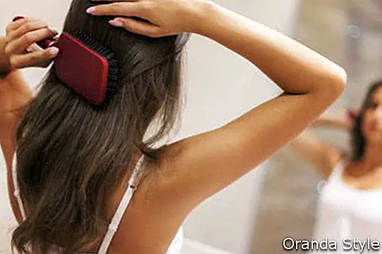 אישה צעירה מצחצחת שיער בריא מול מראה