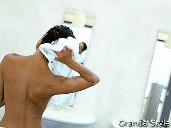 Hermosa mujer joven con bata de baño limpiando su cabello mojado con una toalla después de la ducha