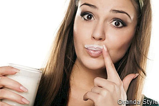 एक हरे रंग की शर्ट में सुंदर खुश लड़की ने दूध पीने वाले एक प्रसन्न इशारे के साथ और एक उंगली से अपना मुंह पोंछ लिया