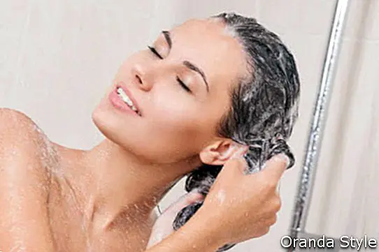 Giovane donna che lava la testa sotto la doccia di shampoo