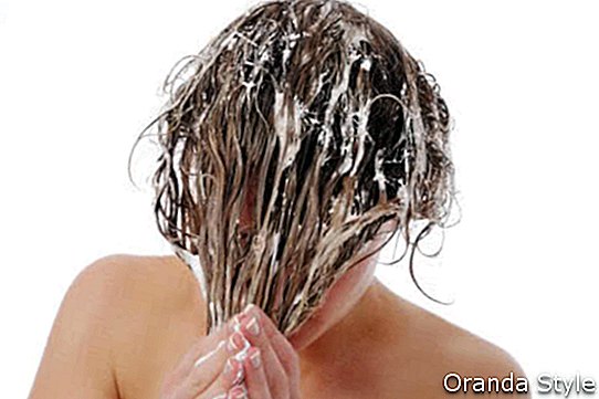 Wanita dengan rambutnya yang basah dan bersabun menutupi wajahnya, mencuci dan mengondisasinya dengan bahu telanjang