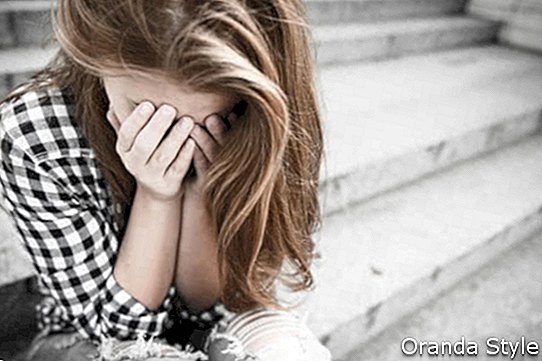 Adolescente depresso infelice con il fronte nella seduta delle mani all'aperto