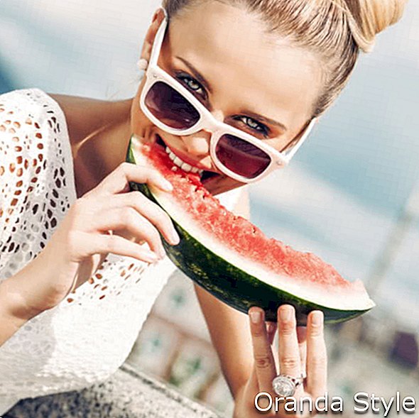 schönes junges Mädchen mit dem Fliegenhaar im weißen Sommerkleid, das Sonnenbrille trägt, beißt saftige Wassermelone